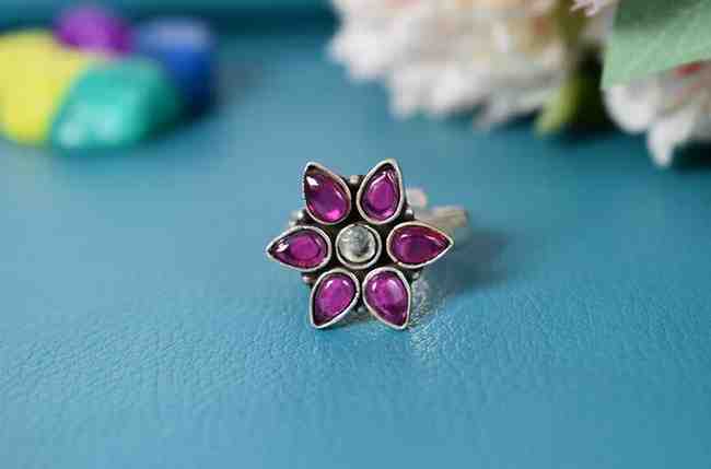 A silver ring with a flower-shaped design featuring pink cutstones and a white center cutstone.