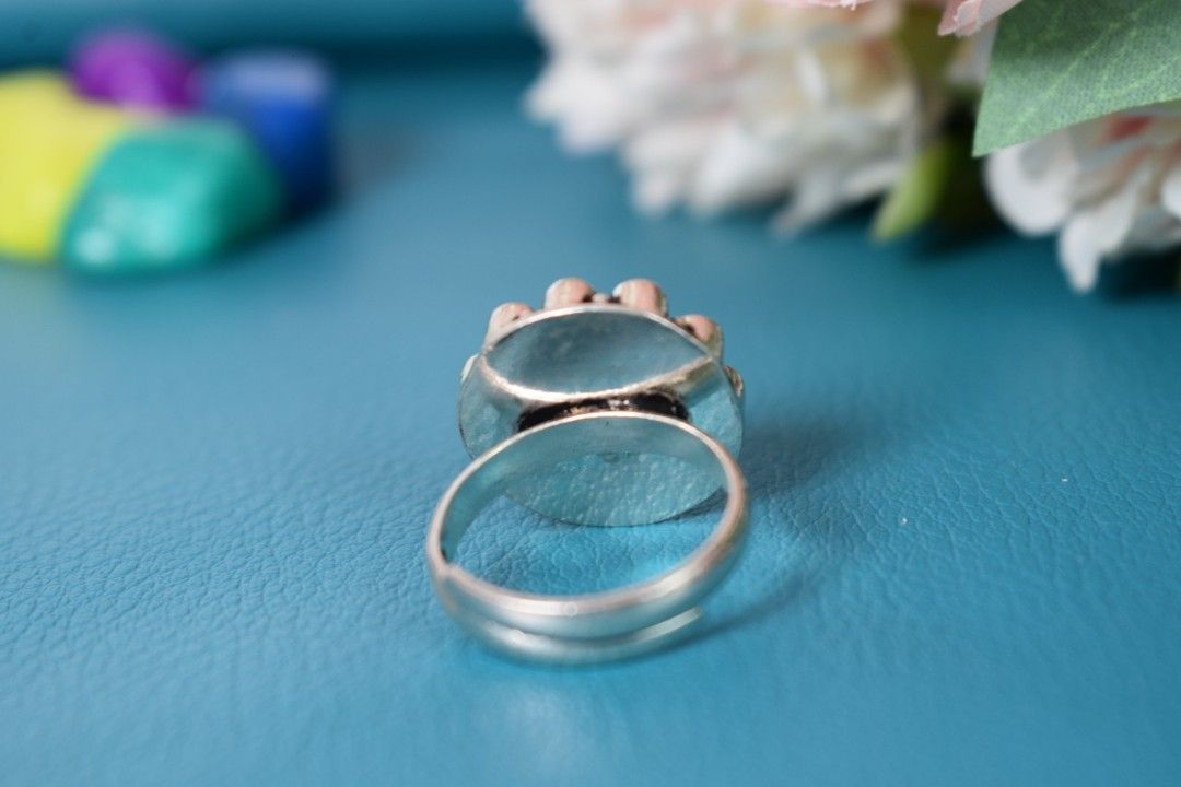 A silver ring with a circular design featuring a red cutstone surrounded by white cutstones.