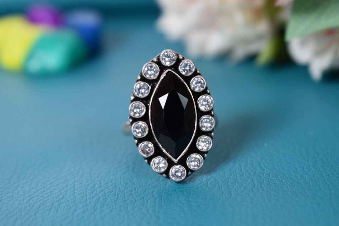 A silver ring with an oval-shaped black cutstone surrounded by white cutstones.