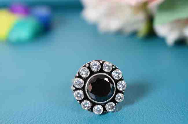 A silver ring with a circular design featuring a black cutstone surrounded by white cutstones.