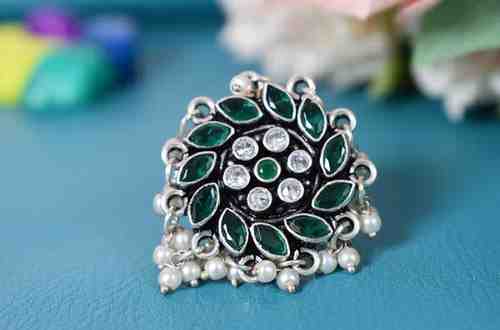 A silver ring with a circular design featuring green and white cutstones, adorned with pearls.