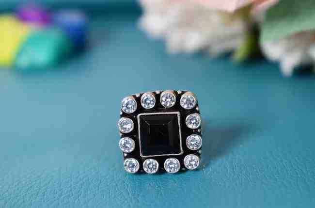 A silver ring with a square-shaped black cutstone surrounded by white cutstones.