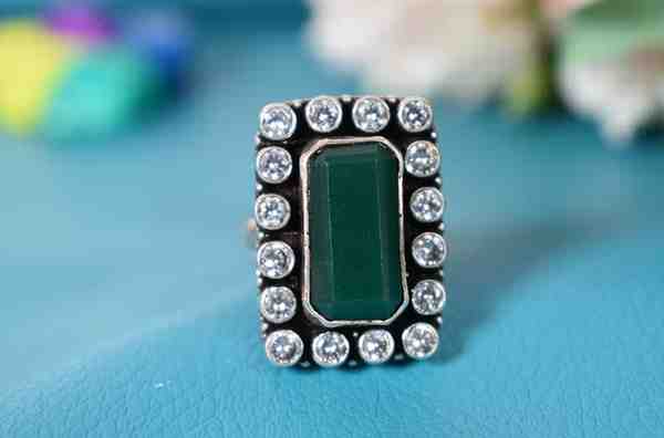 A silver ring with a rectangular green cutstone surrounded by white cutstones.