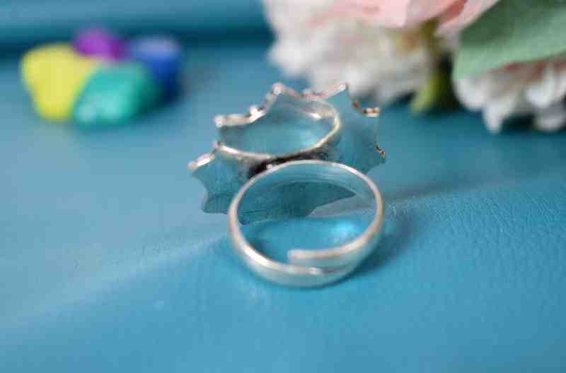 A silver ring featuring a floral design with a red cutstone surrounded by green cutstones.