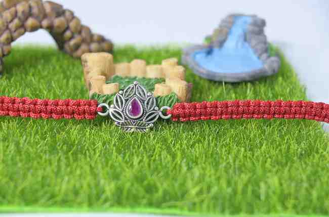 A 925 sterling silver Rakhi featuring an intricate design with a central red stone for Raksha Bandhan.