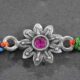 A silver Rakhi featuring an amazing floral design with a colorful center stone.