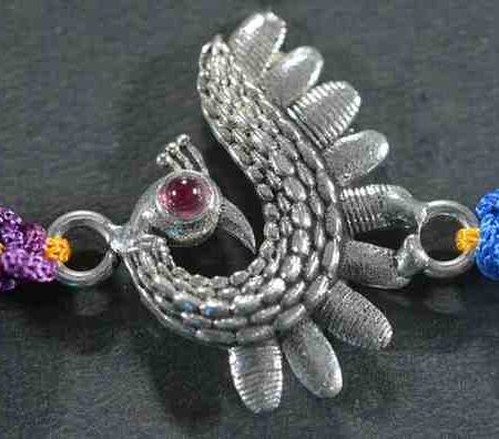 A silver Rakhi featuring a vibrant peacock design.