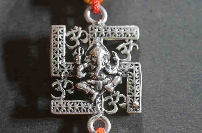 A silver Rakhi featuring Lord Ganesh seated on a Swastik symbol.