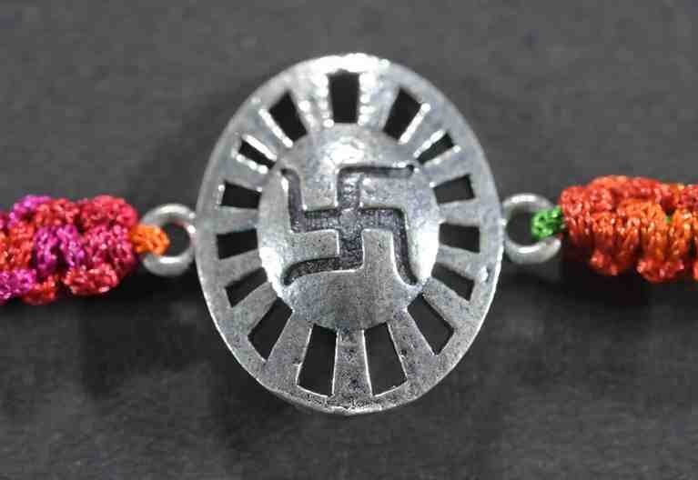 A silver Rakhi featuring an oval shape with a divine Swastik design.