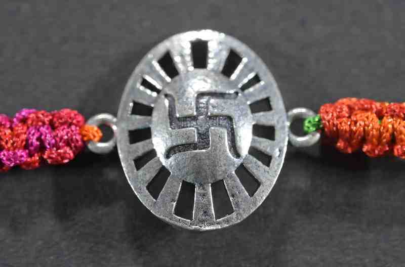 A silver Rakhi featuring an oval shape with a divine Swastik design.