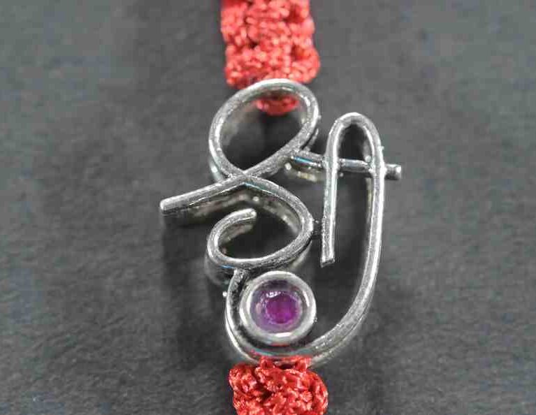 A silver Rakhi featuring the word "Shree" adorned with cutstone embellishments.