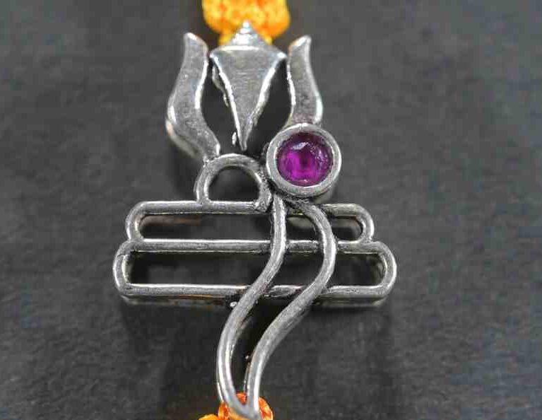A silver Rakhi featuring intricate designs of Lord Shiva's Tripund (three horizontal lines) and Trishul (trident).