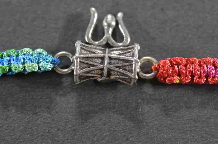 A silver Rakhi featuring intricate designs of Lord Shiva's Damru and Trishul